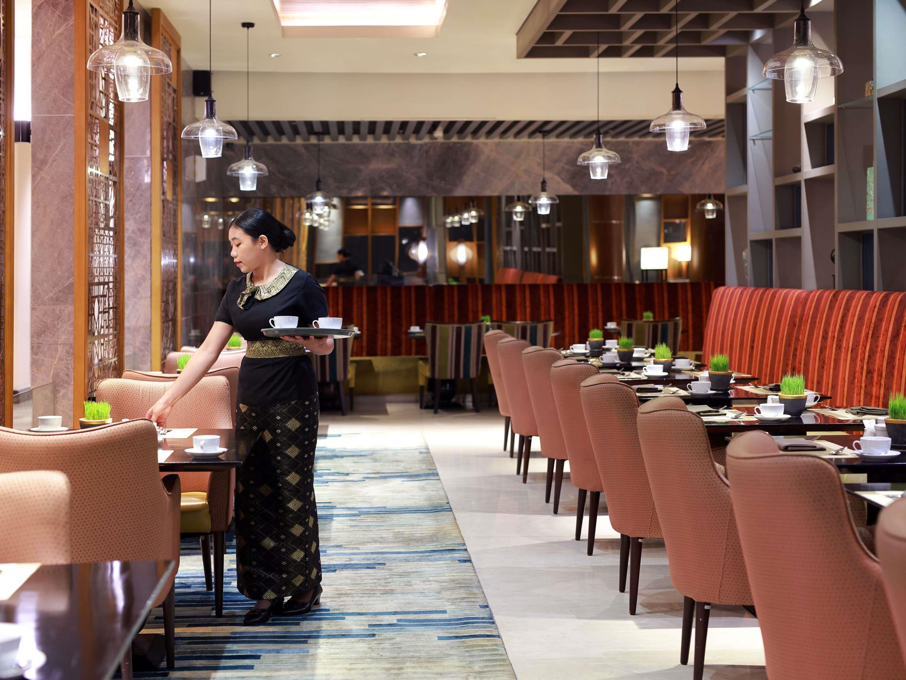 Ein Restaurant mit einem langen Tisch, mehreren Stühlen und hängenden Pendelleuchten.