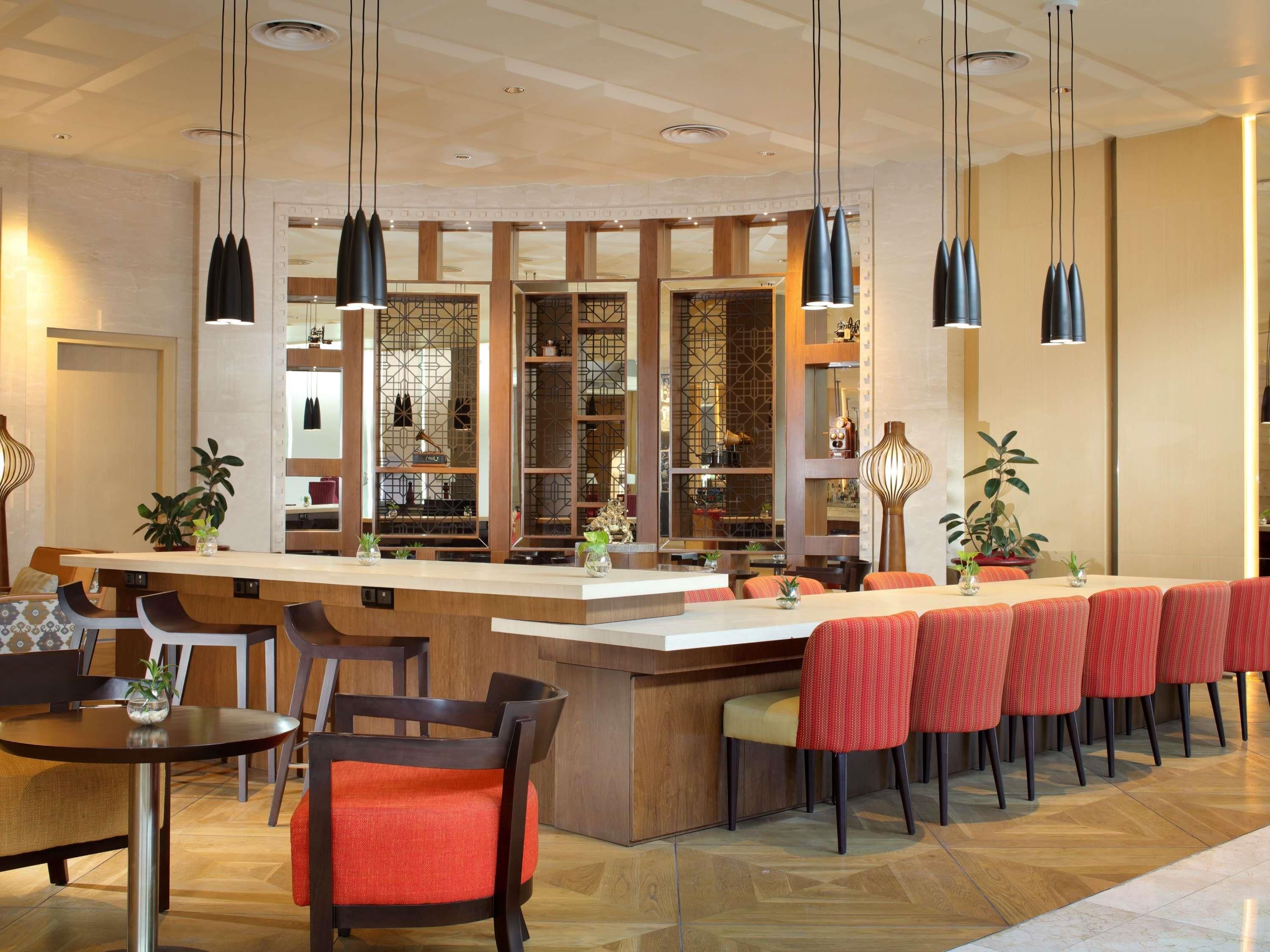 A modern bar area with a long counter, multiple seating options, and pendant lighting.