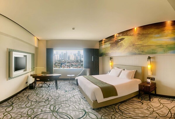 Habitación de hotel con una cama grande, un escritorio, una silla, un televisor y vistas a la ciudad.
