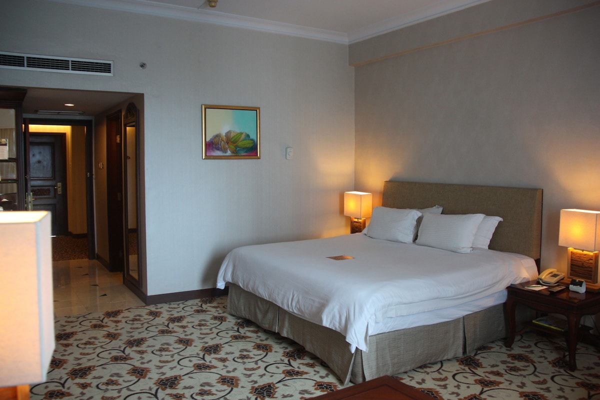Una habitación de hotel con una cama grande, dos lámparas de noche, un teléfono y un cuadro en la pared.
