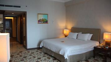 A hotel room with a large bed, two bedside lamps, a telephone, and a painting on the wall.