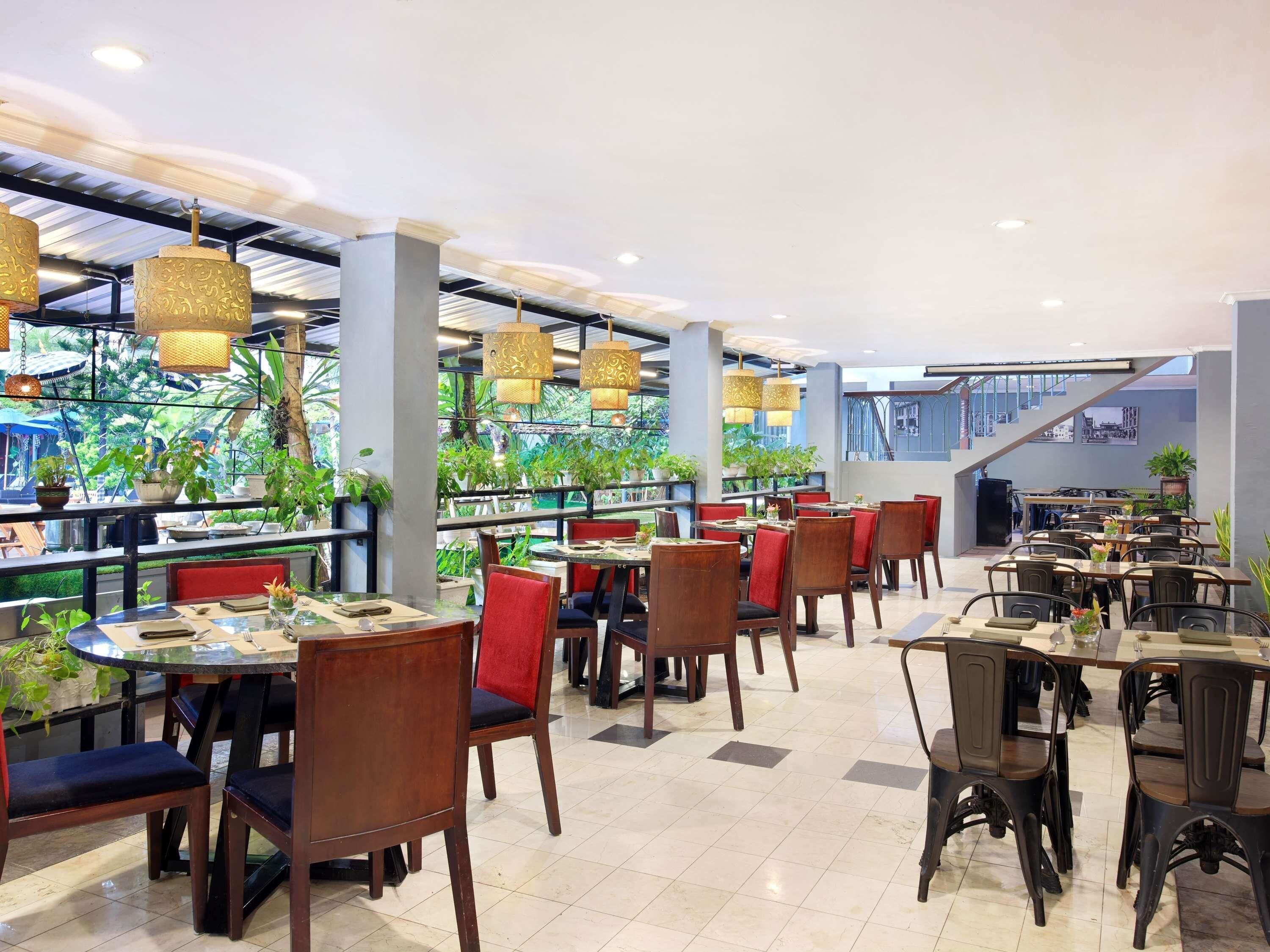 A restaurant with multiple dining tables, chairs, hanging lights, and potted plants.