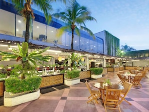 An outdoor restaurant area with tables and chairs, surrounded by potted plants and palm trees. - Grand Mercure Medan Angkasa (Medan)