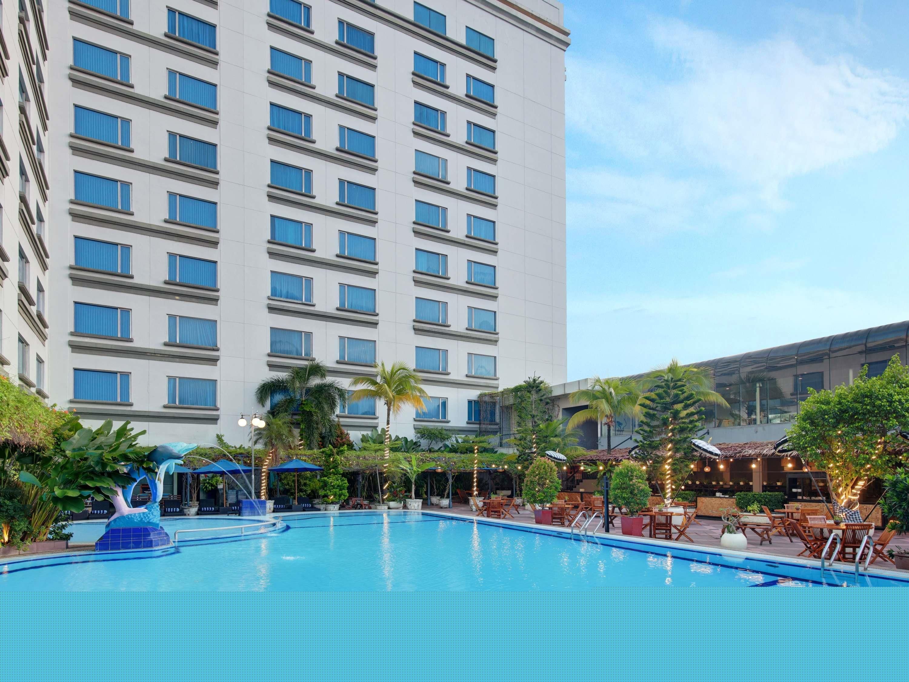 A hotel with a large pool, outdoor seating, and a tall building with many windows.