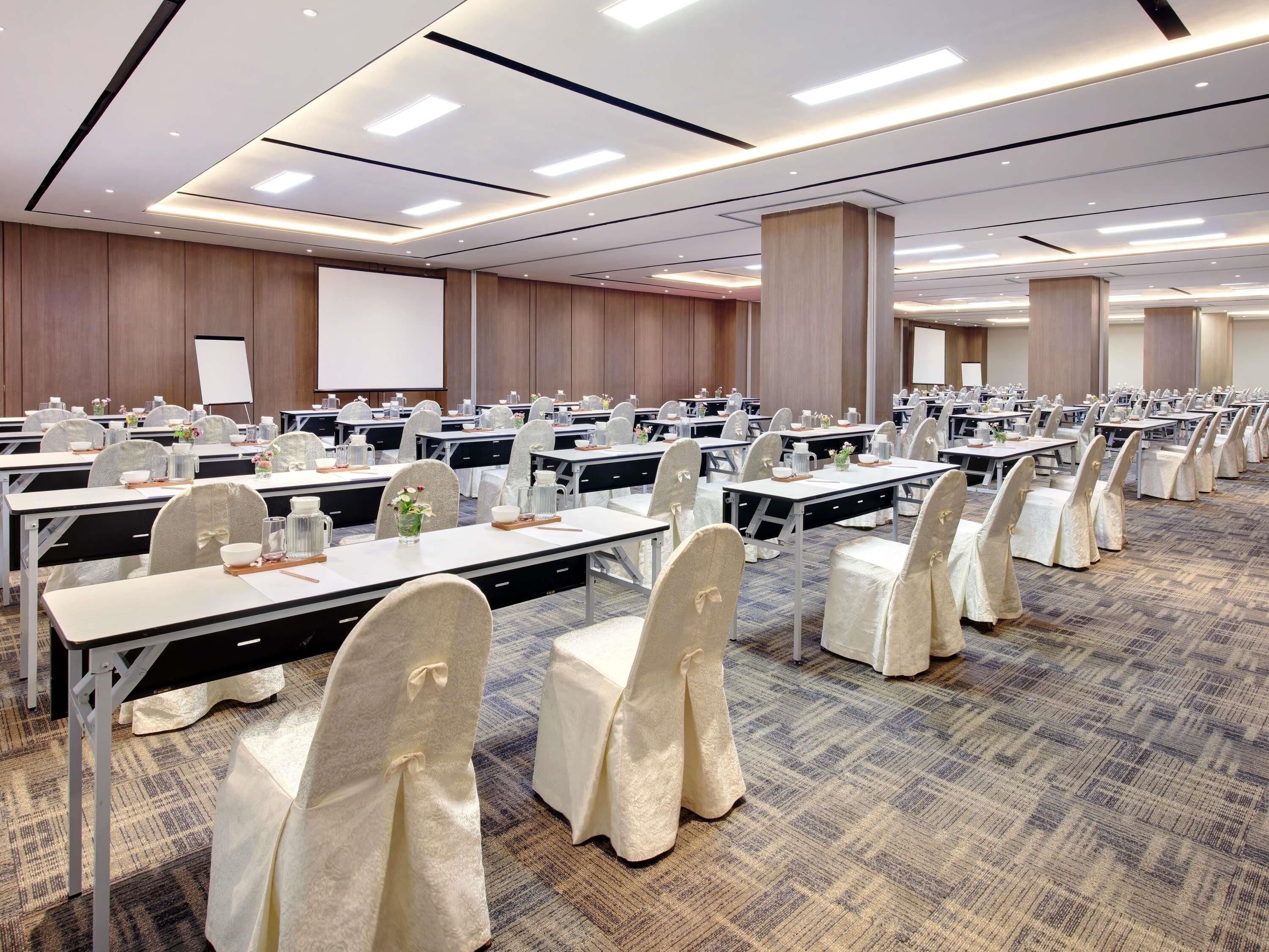 A conference room with multiple tables, chairs, and a projector screen.