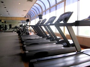 Varias caminadoras en un gimnasio con ventanas amplias y un techo alto.