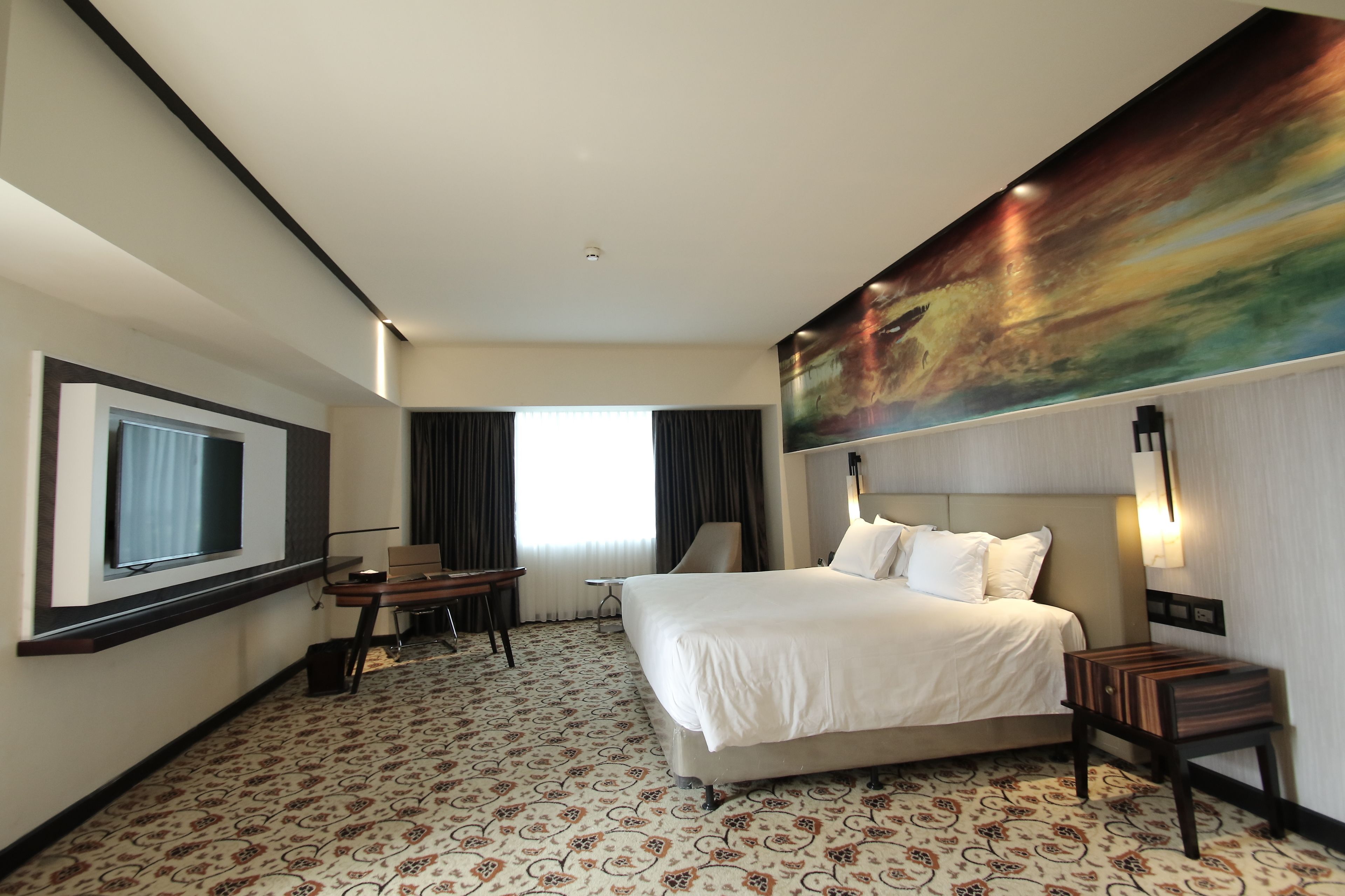 A hotel room with a large bed, a desk, a chair, a TV, and a painting on the wall.
