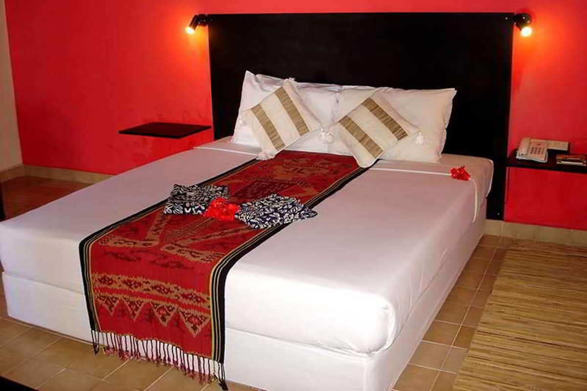 Un lit bien fait, recouvert d’une couverture à motifs rouges et blancs, avec des oreillers blancs et une décoration florale rouge.