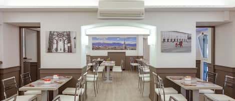 Uma sala de jantar com várias mesas e cadeiras, um quadro grande representando uma paisagem urbana e um aparelho de ar condicionado.