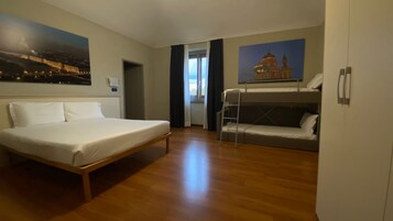 Hotellihuone, jossa on sänky, kerrossänky, puulattia ja kaksi taulua seinillä.