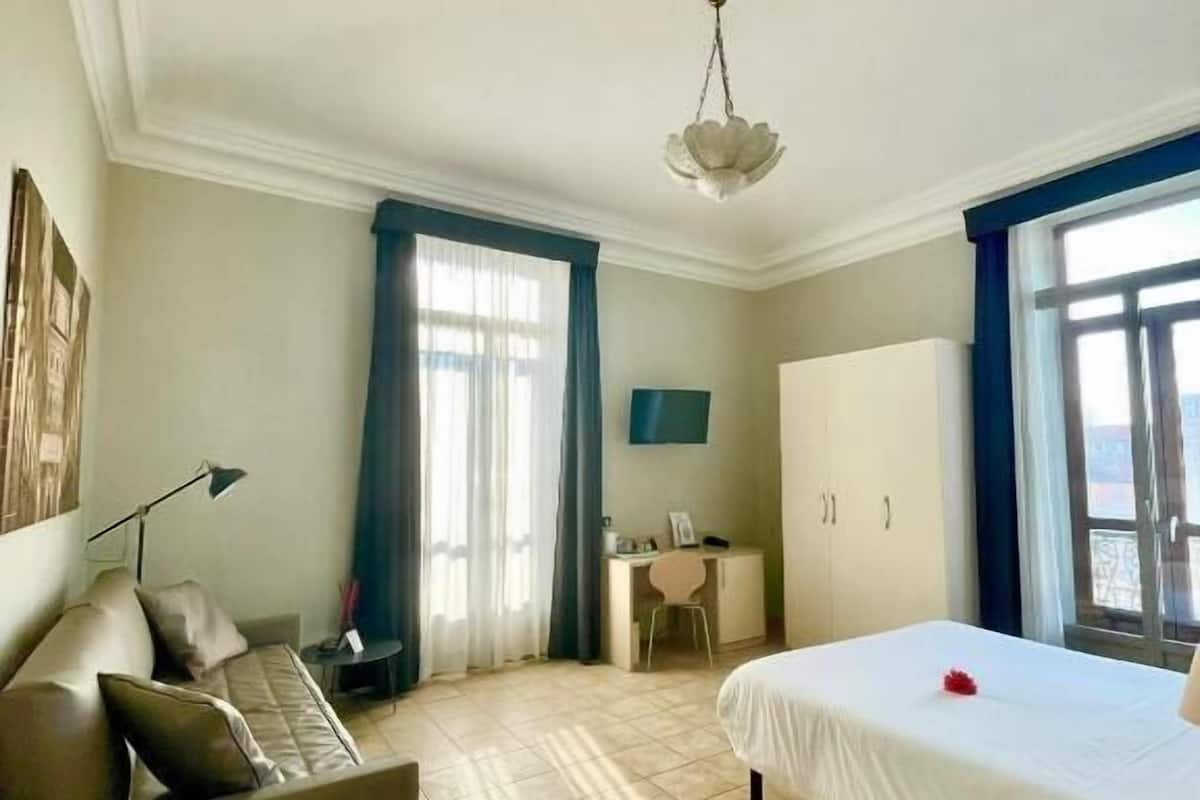 A hotel room with a bed, a desk, a chair, a sofa, and a wardrobe.