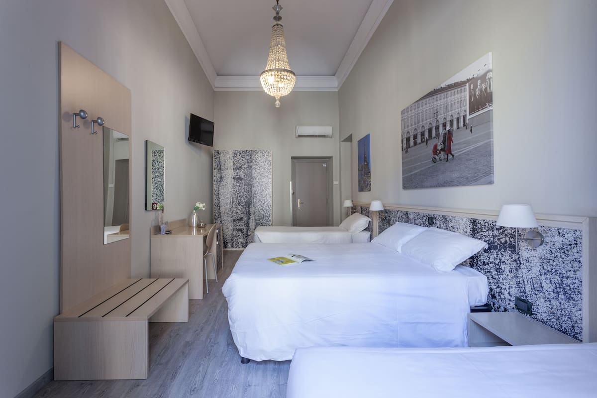 A modern hotel room with a large bed, a bench, a desk, and a mirror.