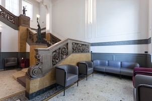 A lobby with a grand staircase, a waiting area with leather chairs, and a tiled floor.