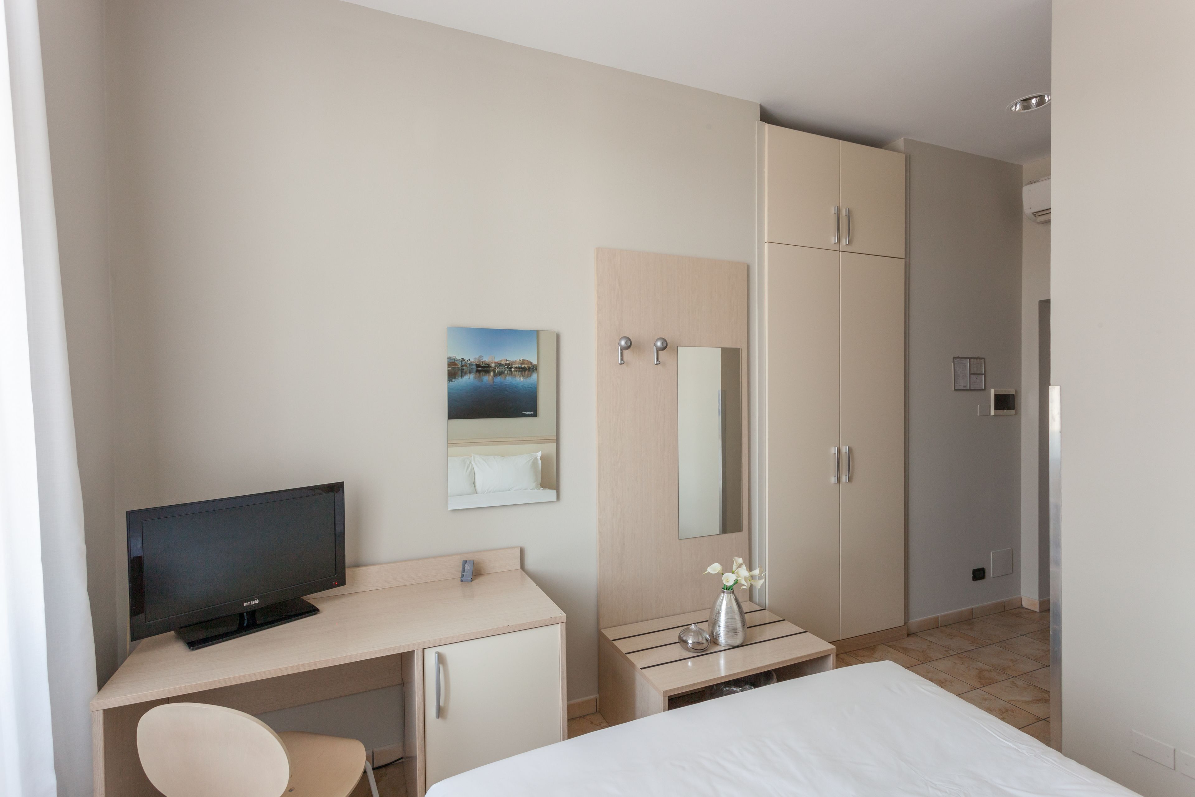Et hotelværelse med seng, skrivebord med fjernsyn, stol, toiletbord med spejl og garderobeskab.