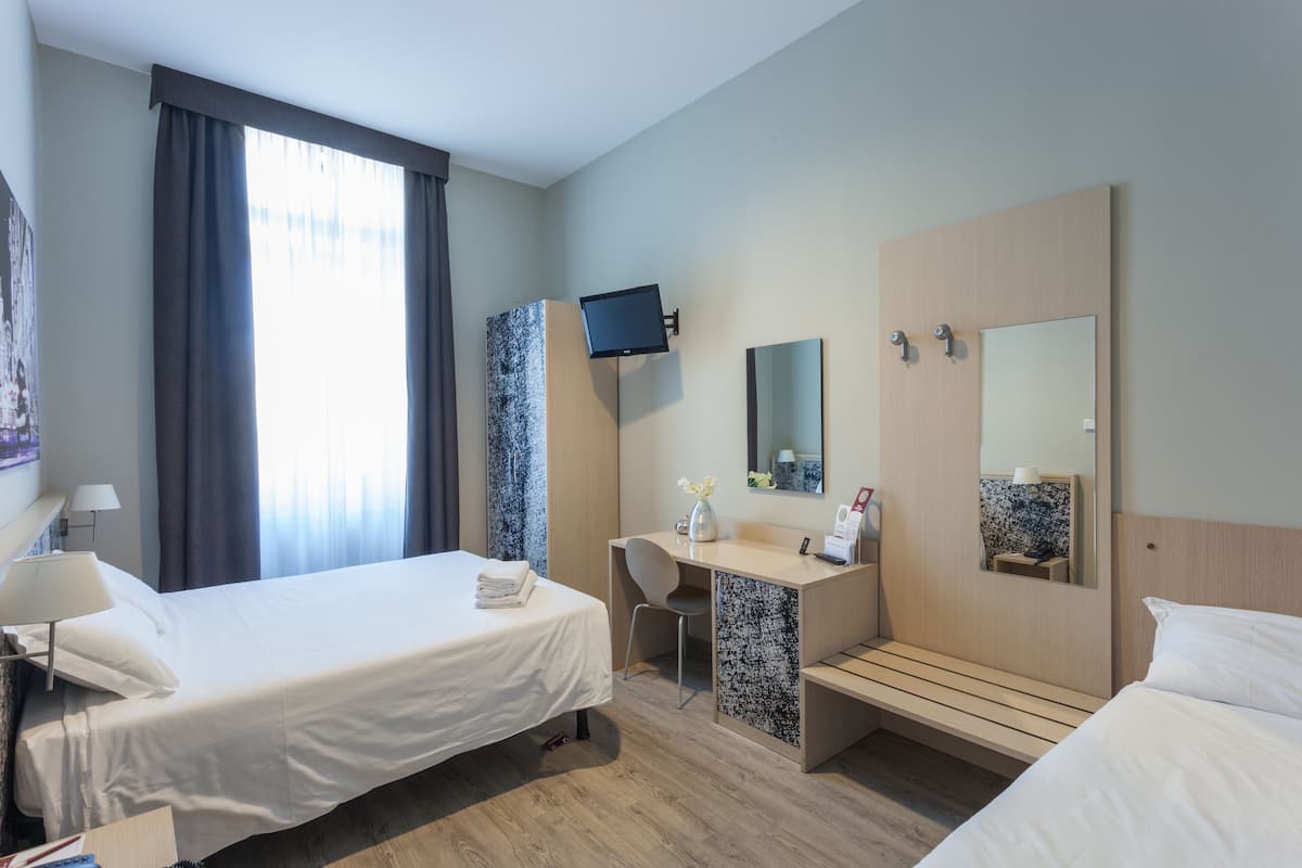 A hotel room with a bed, desk, chair, and a TV mounted on the wall.