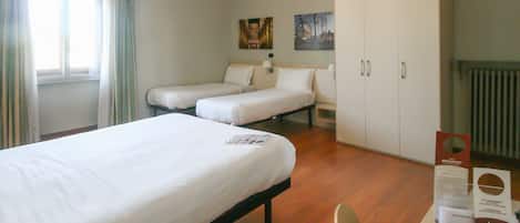 A hotel room with two single beds, a wooden floor, a large wardrobe, and a window with curtains.