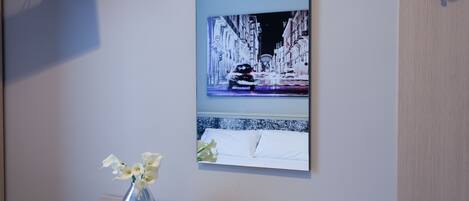 Ein Hotelzimmer mit einem Bett, einer Blumenvase, einem Gemälde einer verschneiten Straße und einem an der Wand befestigten Fernseher.