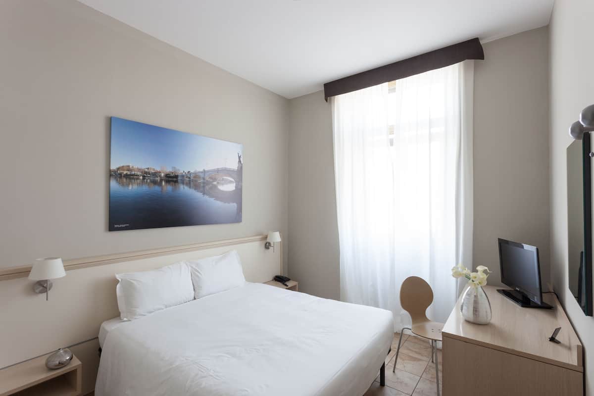 A hotel room with a large bed, a desk with a computer, a lamp, and a painting on the wall.