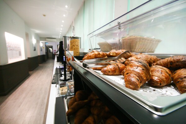 A buffet line with various baked goods, including croissants and bread, displayed in a glass case.