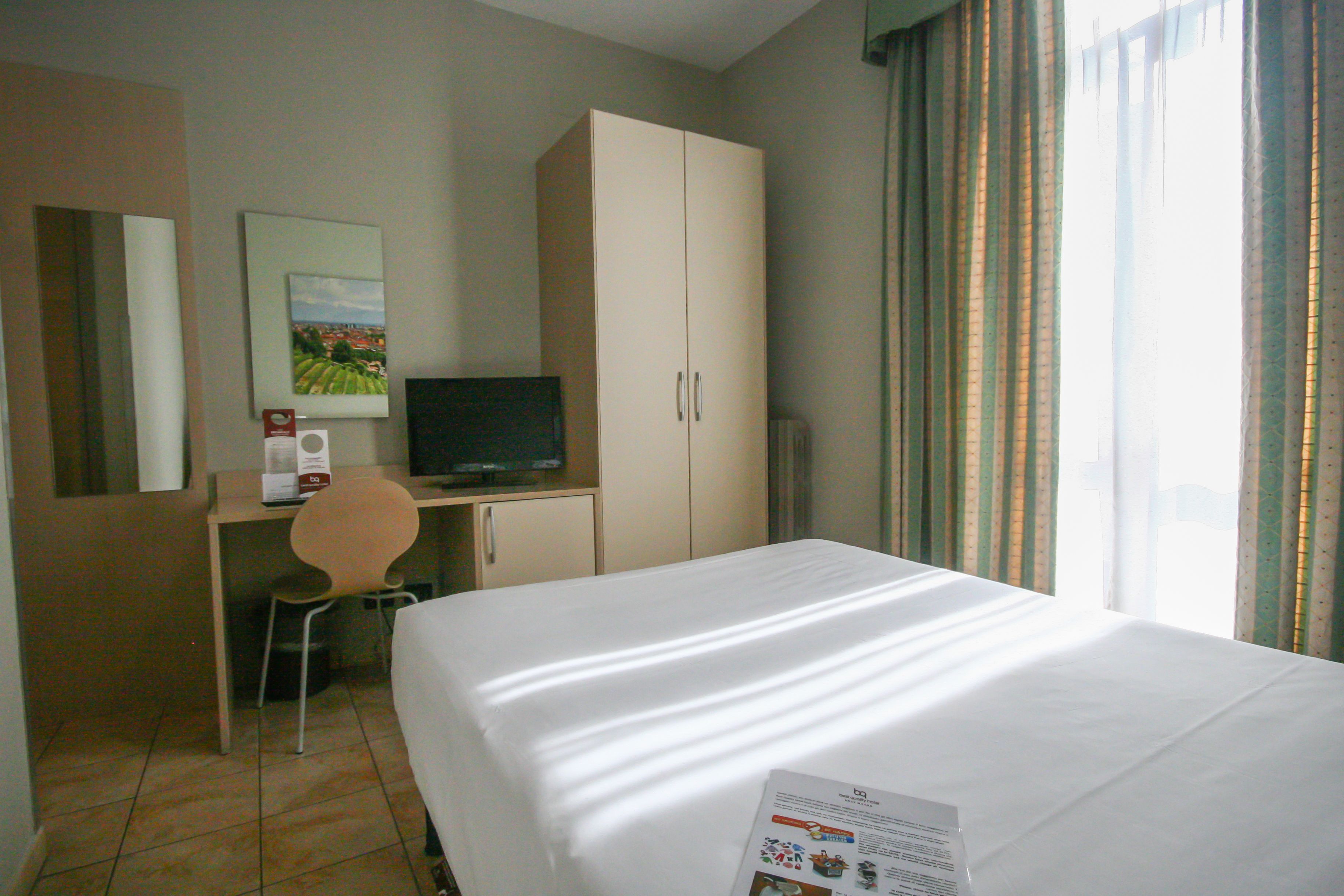 Una habitación de hotel con una cama, un escritorio con una silla, un televisor y un armario.