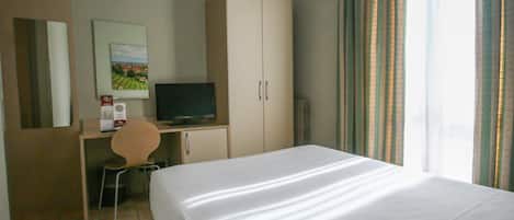 A hotel room with a bed, a desk with a chair, a television, and a wardrobe.
