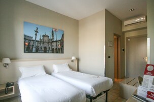Une chambre d’hôtel avec deux lits simples, un tableau représentant un bâtiment accroché au mur, un téléphone sur la table de chevet et une pancarte avec du texte sur la porte.