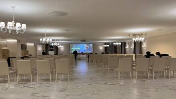 A conference room with rows of white chairs, a large screen at the front, and chandeliers on the ceiling.