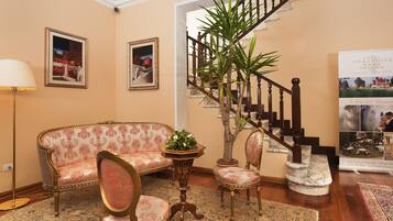 A lobby with a sofa, chairs, a potted plant, a staircase, and a poster.