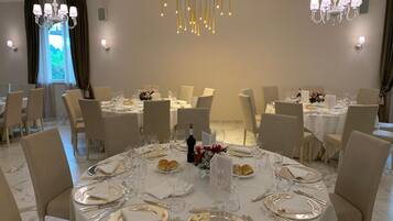 A dining area with round tables set for a meal, featuring white tablecloths, gold-rimmed plates, and silver cutlery.