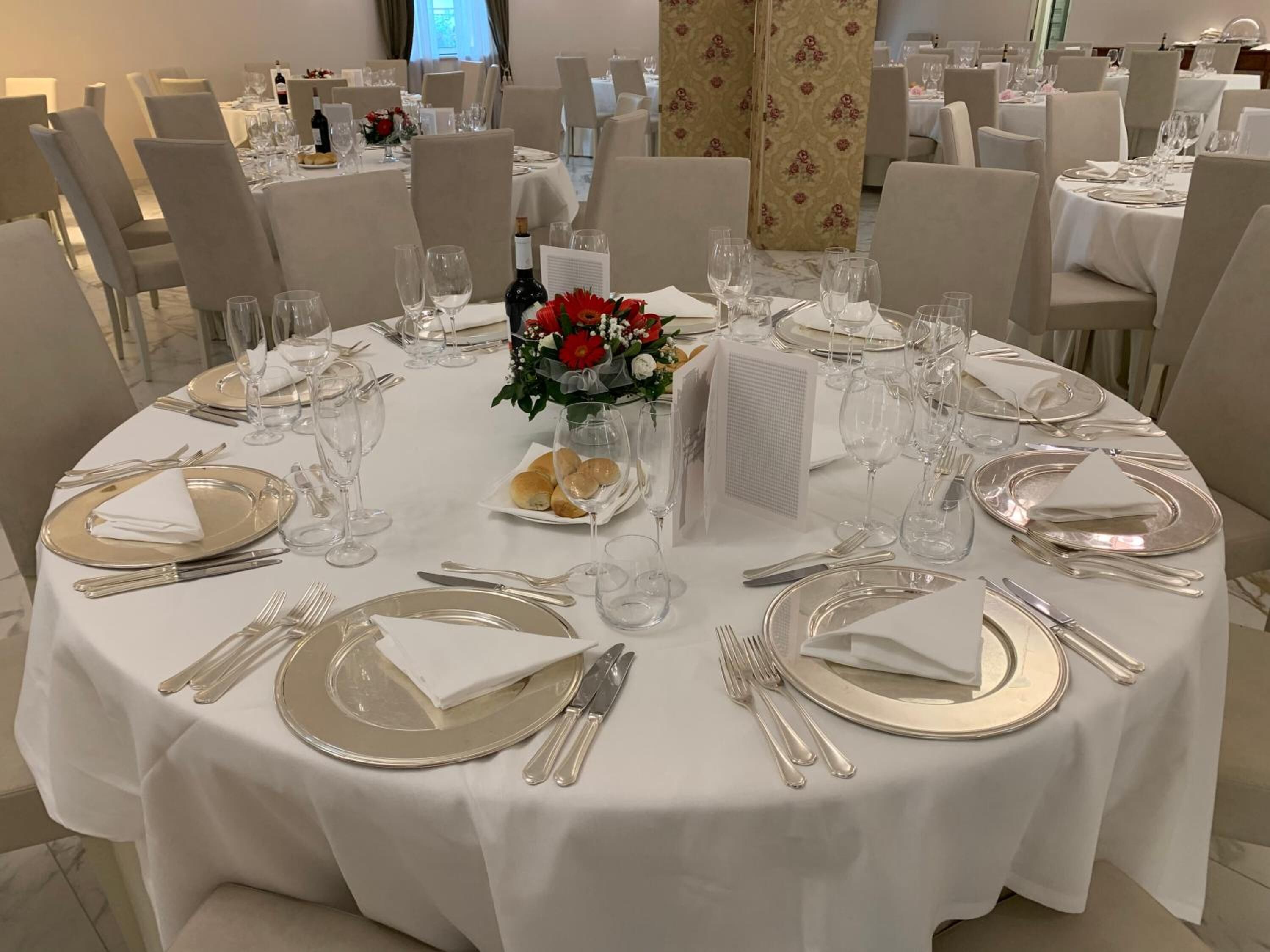 A round dining table set for a formal meal with white tablecloths, silverware, and wine glasses.