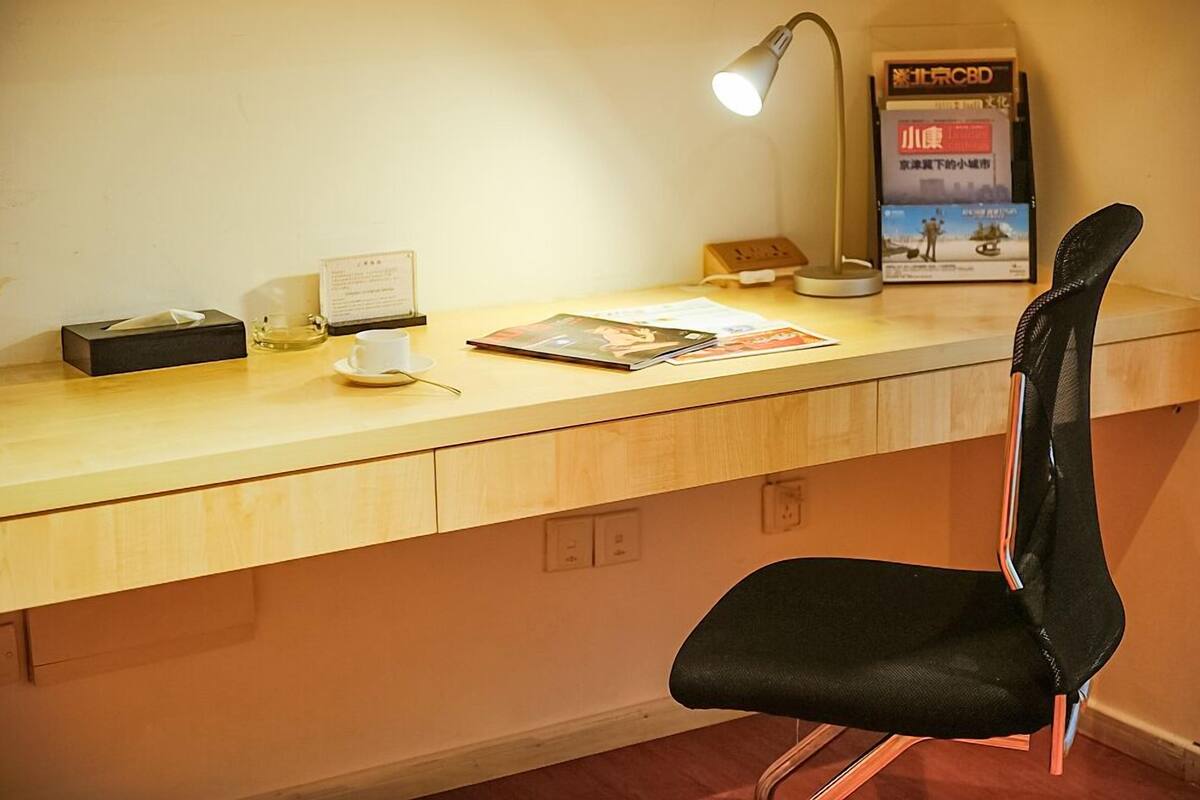 A wooden desk with a black chair, a desk lamp, a tissue box, a small bottle, and some papers.