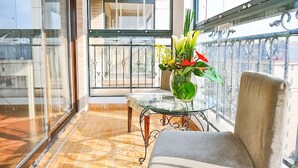 A balcony with a glass door, a small table with a vase of flowers, and a cushioned chair. - Eastern Garden Service Apartment (Shanghai)
