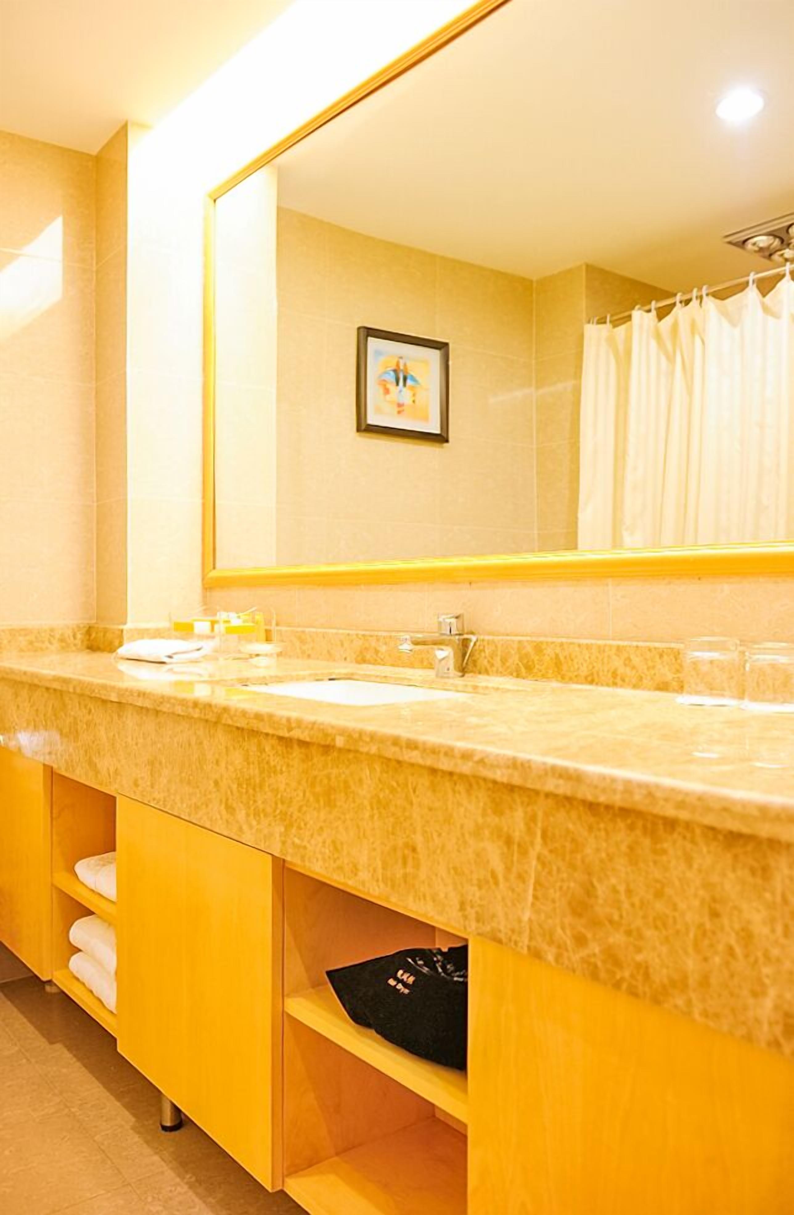 Une salle de bain d’hôtel avec un lavabo en marbre, un grand miroir et un tableau encadré au mur.
