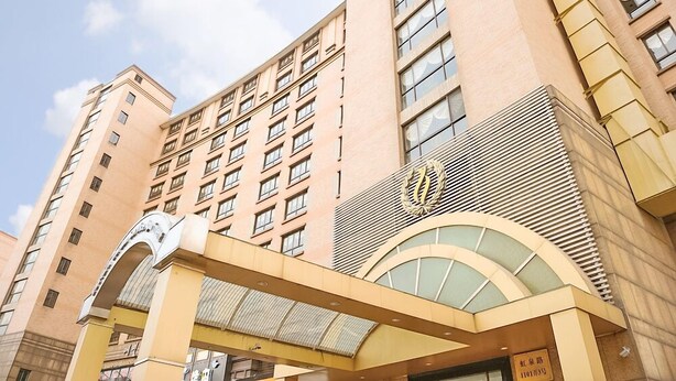 A multi-story hotel with a prominent entrance featuring a large archway and a decorative emblem. - Eastern Garden Service Apartment (Shanghai)