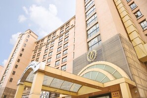 A multi-story hotel with a prominent entrance featuring a large archway and a decorative emblem. - Eastern Garden Service Apartment (Shanghai)