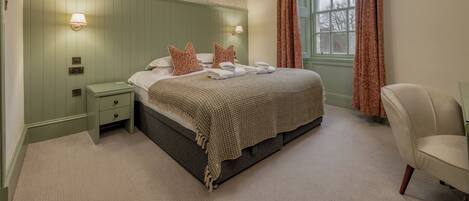 A bedroom with a bed, nightstands, a chair, a window with curtains, and wall-mounted lights.
