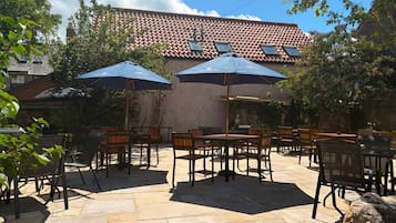 Ein Außenbereich mit einer Terrasse, Steinböden, Tischen, Stühlen und Sonnenschirmen.