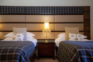 Habitación de hotel con dos camas, una mesita de noche, una lámpara y un cabecero con diseño escocés.