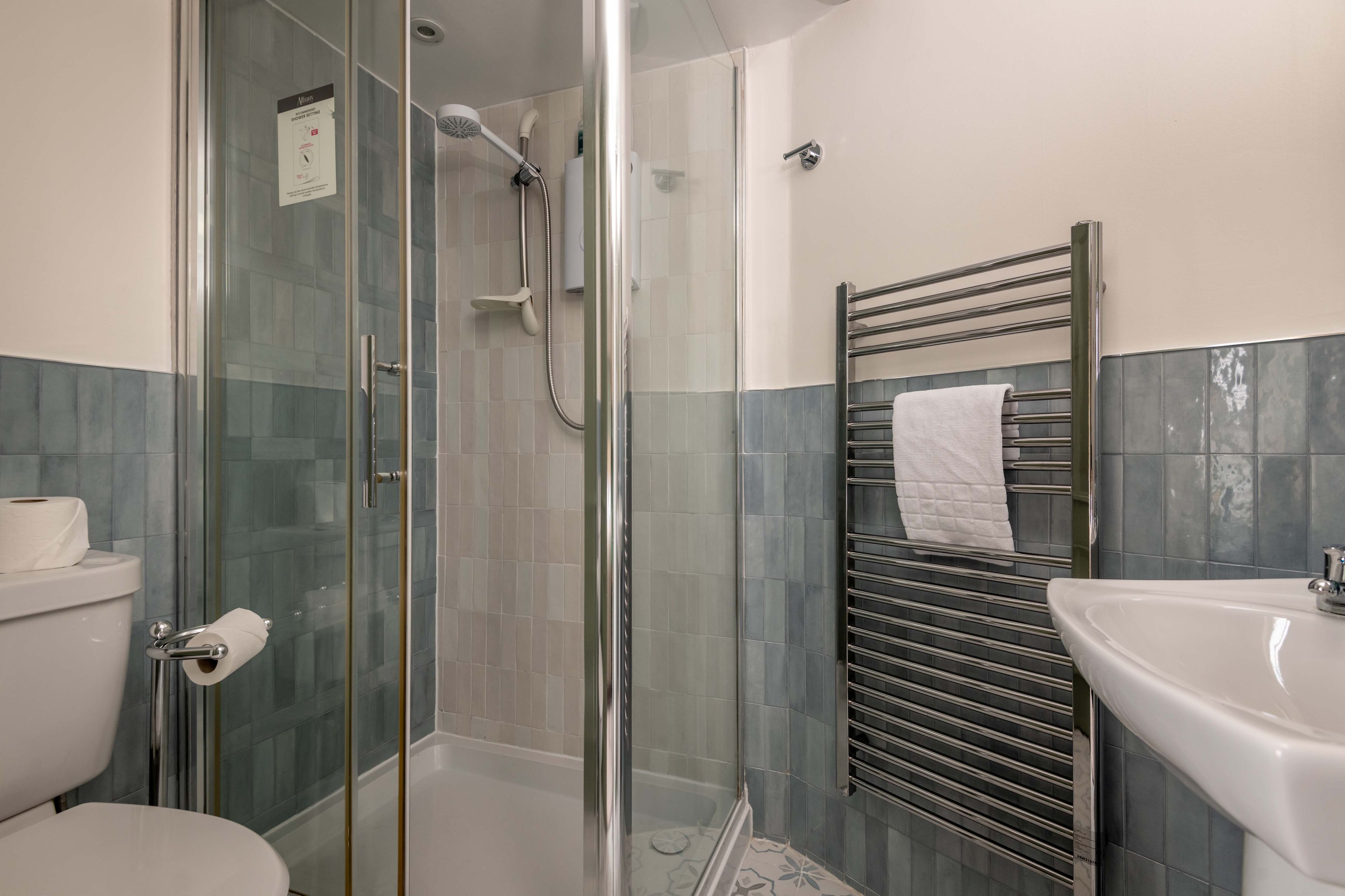 Un baño con ducha envuelta en vidrio, un inodoro, un lavabo y un perchero para toallas.