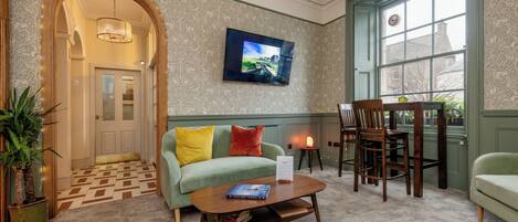 A cozy room with a green sofa, a wooden coffee table, and a TV mounted on the wall.