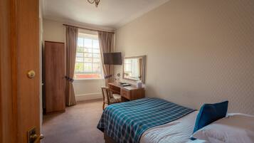 A hotel room with a bed, a desk with a computer, a chair, a television, and a window with curtains.