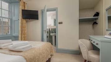Habitación de hotel con cama, televisor montado en la pared, baño visible a través de una puerta abierta y tocador con espejo.