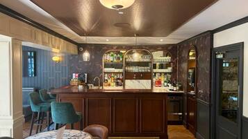 A bar area with a marble-topped table, green upholstered chairs, and a bar counter stocked with bottles.