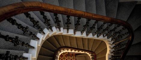 Eine Wendeltreppe mit Holzgeländer und weißen Spindeln, die zu einer Empore mit einem gemusterten Boden und einer kleinen Sitzecke führt.