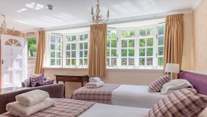 Une chambre d’hôtel avec deux lits, un bureau, une chaise et une vue sur la verdure grâce à de grandes fenêtres.