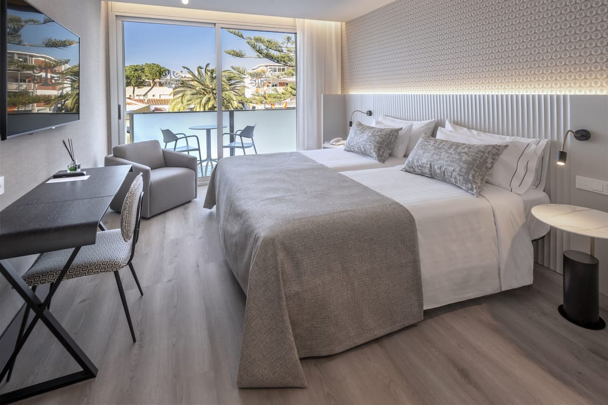 A modern hotel room with a large bed, a desk with a chair, a small table, and a view of the outdoors.