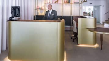 Un área de recepción de hotel moderna con un mostrador grande e iluminado, una zona de estar con una mesa de madera y un estante decorativo con varios objetos.
