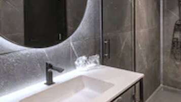 Un baño moderno con un espejo grande, un lavamanos y una ducha.