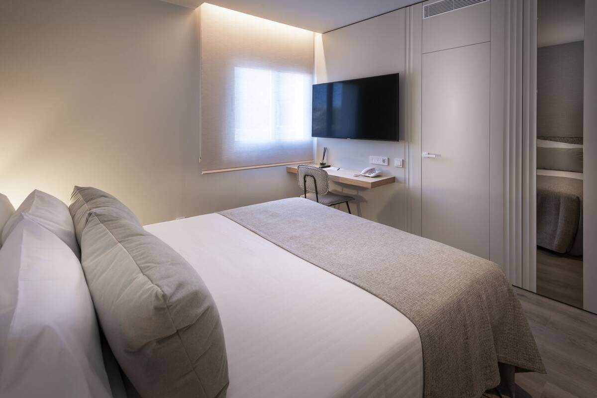 A modern hotel room with a large bed, a desk, and a TV mounted on the wall.