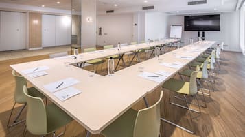 Un salón de conferencias con una larga mesa, sillas, una pantalla de proyector y una pizarra.